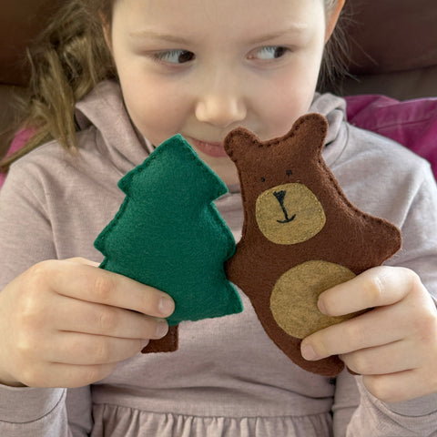 Child holding a green felt tree and brown bear toy
