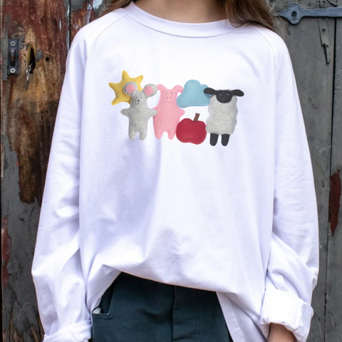 White shirt with farm animal designs worn by a girl against a rustic wooden background.