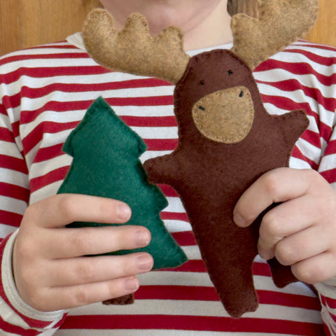 Child holding a felt moose and tree toy against a striped shirt background