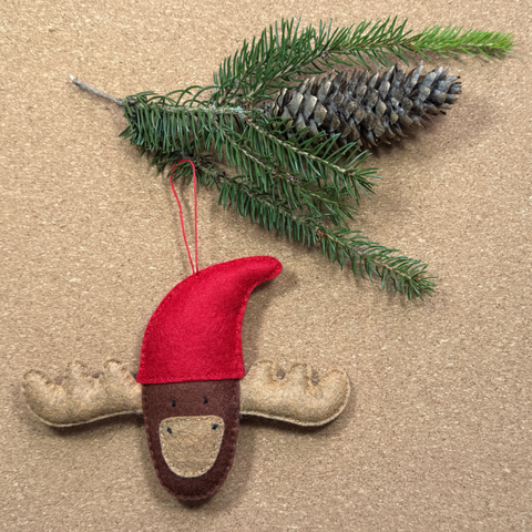 Decorative moose ornament with red hat and green branch on cork background