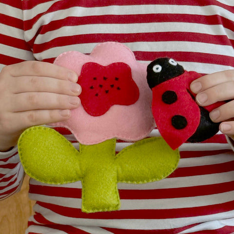 Child holding a pink flower AND ladybug toy against a red and white striped shirt.