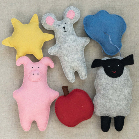 Set of colorful felt animal toys including a sun, mouse, pig, and sheep, cloud, and apple on a beige background.