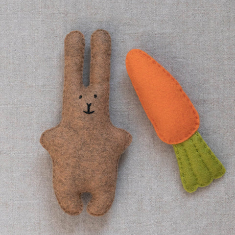 Felt brown bunny toy with a carrot on a neutral fabric background