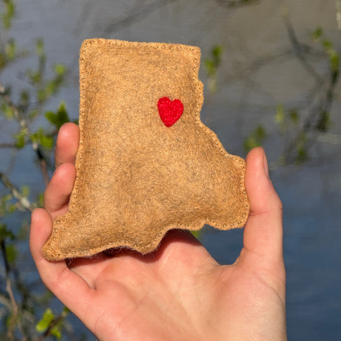 Hand holding a felt diy rhode island with a red heart shape against a natural background