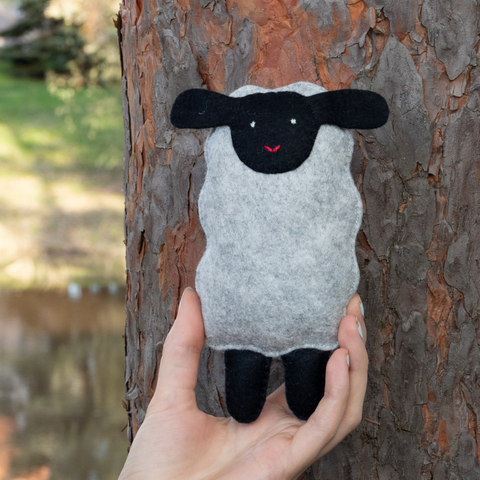 Hand holding a small sheep plush toy against a tree