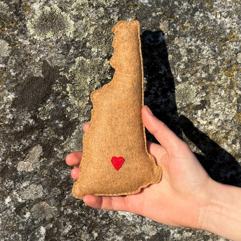 Hand holding a brown fabric object with a red heart on a textured stone surface