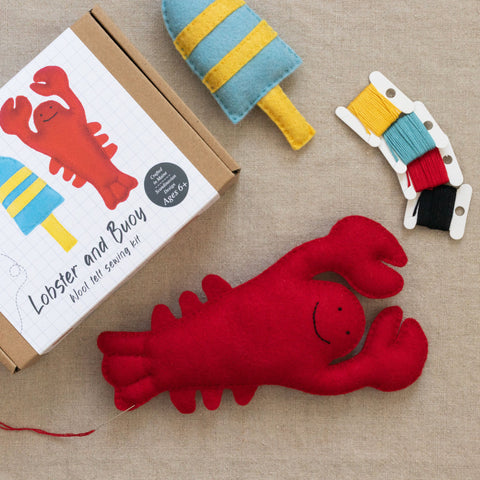 Red lobster and buoy felt toys with sewing kit packaging and threads on a neutral background