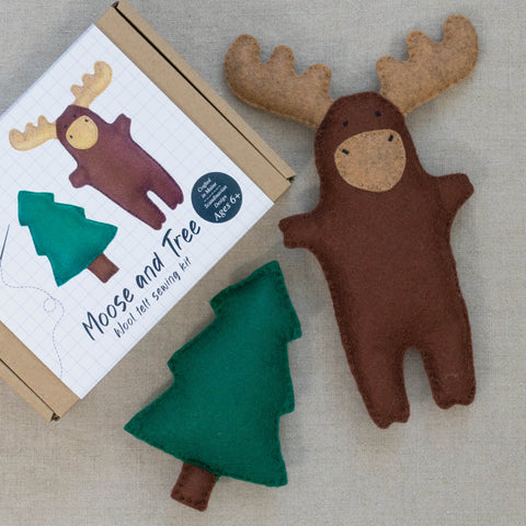 Felt moose and tree felt toys next to packaging a neutral background