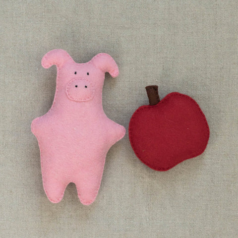 Pink felt pig and red apple on a neutral fabric background