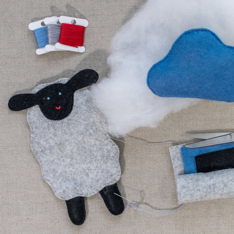 Handmade felt sheep toy with wool and thread spools on a neutral surface