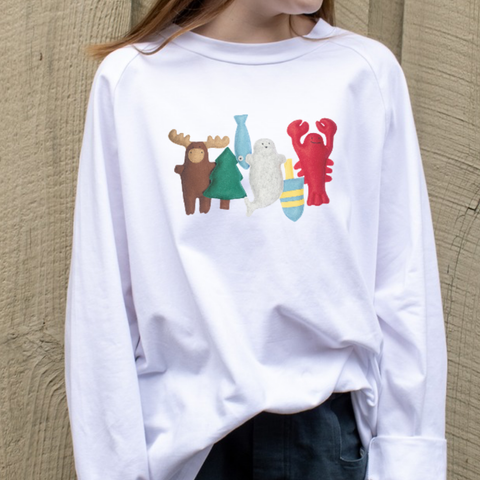 White sweatshirt with colorful wild north animal graphics worn by a girl against a neutral wall.