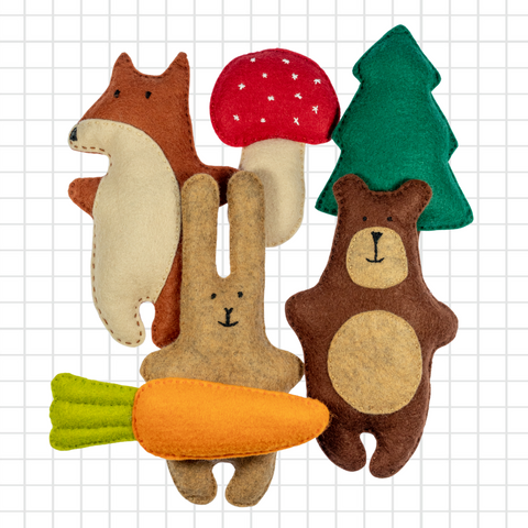 Set of felt animal toys including a bear, rabbit, squirrel, mushroom, and carrot on a grid background.