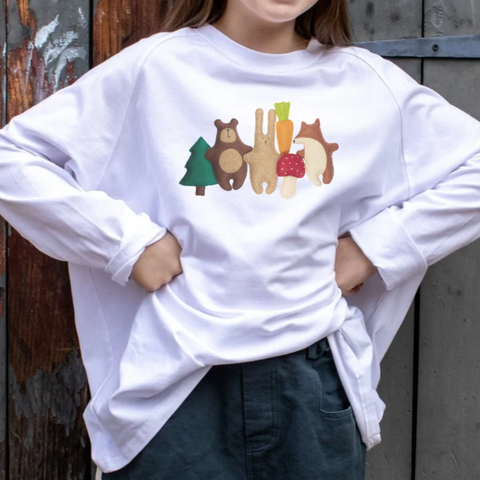 Girl wearing a white shirt with woodland animal designs against a rustic wooden wall.