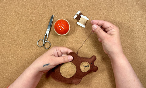 Hands sewing a soft felt animal, symbolizing mindfulness and the mental health benefits of hand stitching.