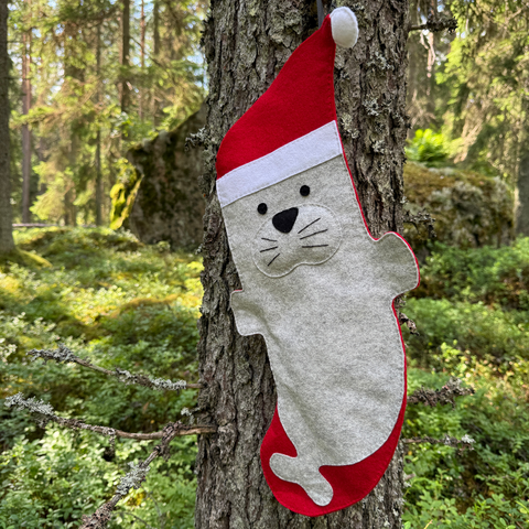 Christmas stocking shaped like a seal with a Santa hat hanging on a tree in a forest.