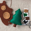 Felt craft materials including a brown bear, green tree, spools of thread, and scissors on a neutral fabric background.