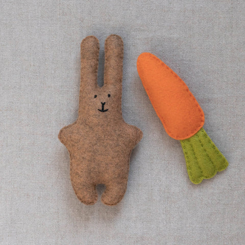 Felt brown bunny toy with a carrot on a neutral fabric background