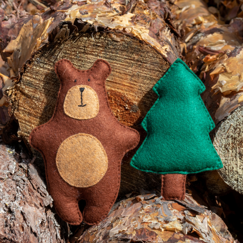 Felt brown bear and green tree toy on a wooden log