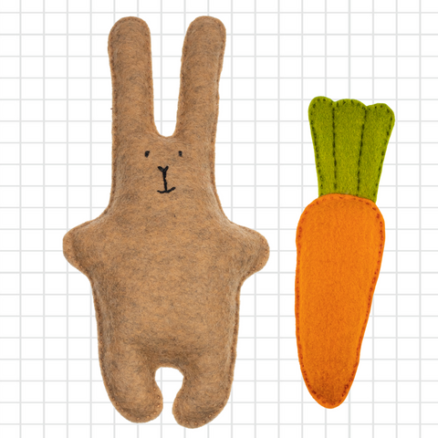 Brown rabbit-shaped toy with a green tail and orange carrot on a grid background