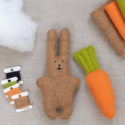 Felt rabbit and carrot toy set on a linen surface with spools of thread.