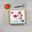 Fox and mushroom needle felt sewing kit packaging on a linen surface with sewing tools.
