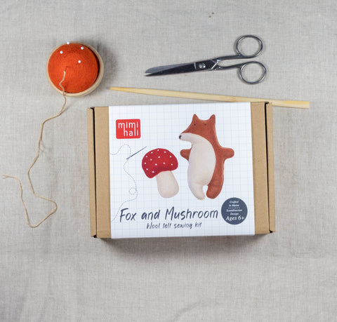 Fox and mushroom needle felt sewing kit packaging on a linen surface with sewing tools.