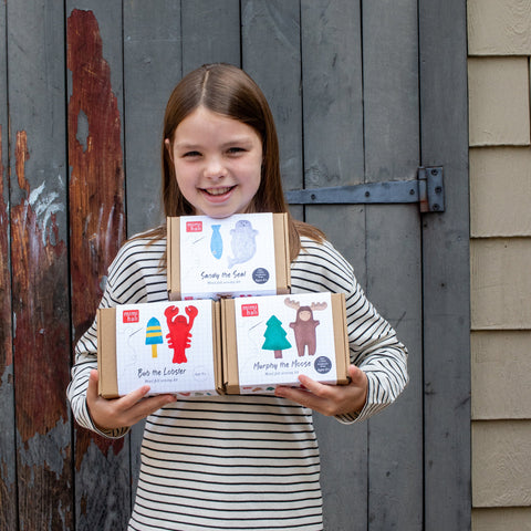 Young girl holding three boxes with colorful labels against a rustic wooden background