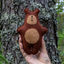 Brown teddy bear held against a tree trunk in a forest setting