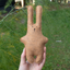 Brown felt bunny toy held in a hand with green foliage in the background
