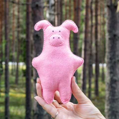 Pink stuffed pig toy held in front of a forest background