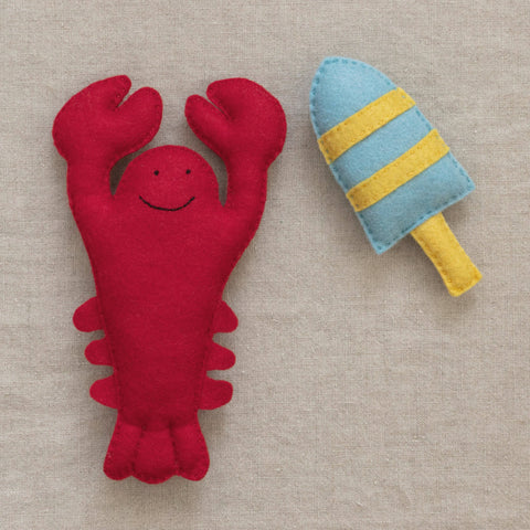 Red lobster plush toy and blue and yellow striped buoy on a neutral background