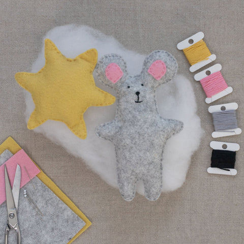 Handmade plush mouse toy with a yellow sun and spools of thread on a linen surface.