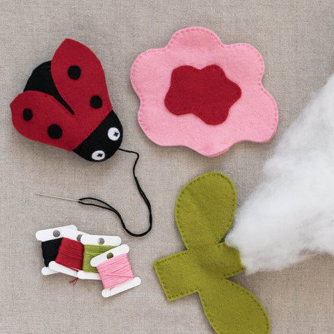 Felt craft items including a ladybug, flower, and sewing materials on a linen surface.