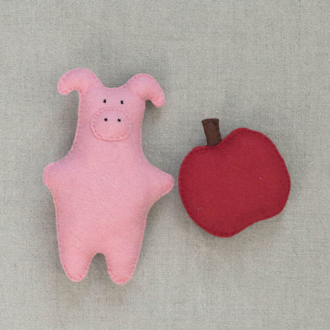 Pink felt pig and red apple on a neutral fabric background