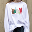 White sweatshirt with colorful wild north animal graphics worn by a girl against a neutral wall.