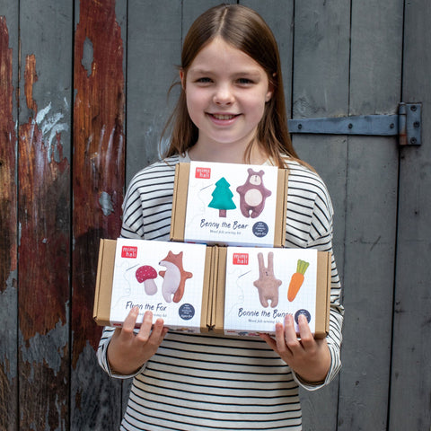 Young girl holding a box of woodland animal kits against a rustic wooden background