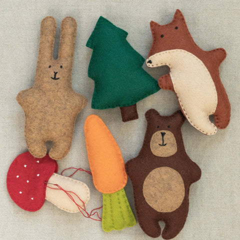 Set of felt animal toys including a bear, bunny, fox, mushroom, carrot and tree on a textured neutral background.